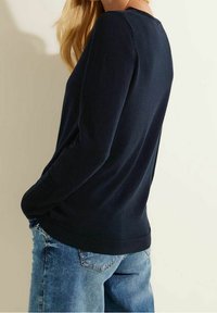 Donkerblauwe trui met lange mouwen, voorzien van een geribde zoom en manchetten, met een zachte textuur en een ontspannen pasvorm. Draagt lichtblauwe spijkerbroek.