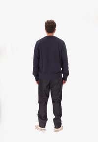 Felpa blu navy con maniche lunghe, polsini e orlo a costine. Abbinate a pantaloni in denim scuro, con una vestibilità rilassata e dettagli di cucitura sottili.