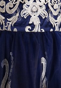 Marindress med silverbroderade blommönster på bodice, med en tüllkjol som har metalltrådsdetaljer.