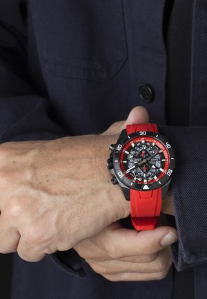 Red and black watch with a rubber strap. Features a detailed face with multiple dials and markers, contrasting colors, and a bold design.