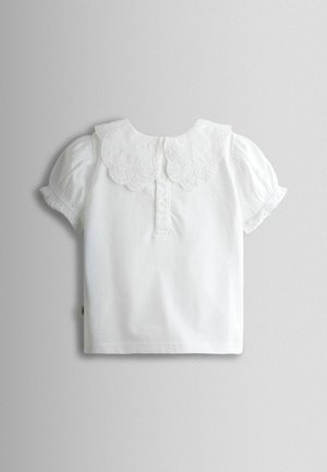 Fehér rövid ujjú ing hullámos csipkegallérral és háromgombos patenttal. Puha anyag, fodros ujjak, minimalista dizájn.