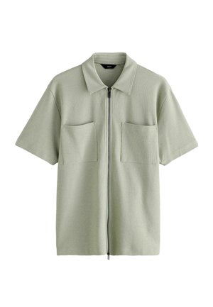 Krótki rękaw, jasnozielona koszula z kołnierzykiem, dwoma naszywanymi kieszeniami z przodu i centralnym zapięciem na zamek błyskawiczny.