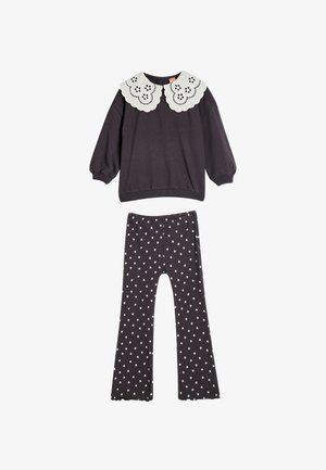 Mørkegrå sweater med en hvid bølget krave og hulmønsterdetaljer, parret med mørkegrå flared bukser med et hvidt hjerte mønster.