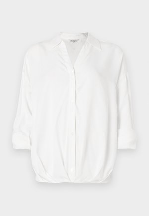 Witte blouse met lange mouwen en kraag, knopen aan de voorkant, en opgerolde mouwen, gepresenteerd tegen een effen achtergrond.