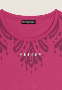 T-shirt rosa brillante con scollatura rotonda, decorata con un motivo astratto in bordeaux scuro e la scritta "FREDDY" stampata in argento metallizzato sul davanti.