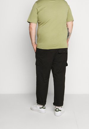 Oliven grøn kortærmet t-shirt, sorte cargo-bukser med sidelommer og hvide sneakers med grønne accenter. Teksturerede bomuldsmaterialer.