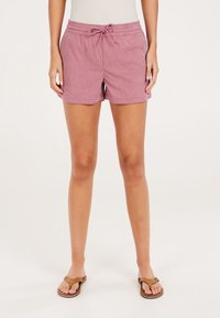 Różowe paskowane szorty z elastycznym paskiem w talii, sznurkiem do wiązania i bocznymi kieszeniami, prezentowane z brązowymi klapkami na neutralnym tle.