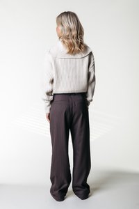 Suéter de punto grueso en crema con un cuello ancho, combinado con pantalones marrones de cuadros. El suéter tiene puños acanalados y un ajuste holgado.