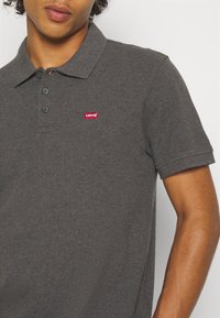 Polo gris en coton, avec un col polo, trois boutons et un petit logo Levi's rouge sur la poitrine gauche.