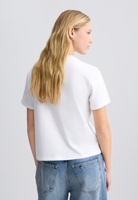 Hvid bomulds T-shirt med en afslappet pasform, korte �ærmer og rund halsudskæring, parret med lyseblå jeans med baglommer.