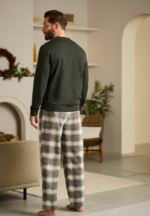 Camisa de manga larga verde oscuro combinada con pantalones de pijama a cuadros en gris claro y marrón. Tejido suave, corte relajado y detalles de costura visibles.