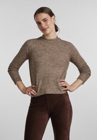 Brown ribbed knit sweater with a high neckline, long sleeves, and a relaxed fit, paired with burgundy corduroy pants.