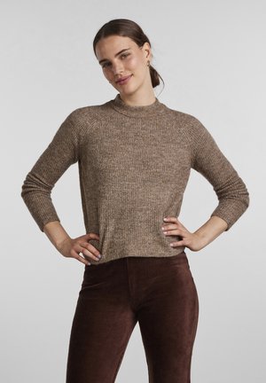 Pull en maille côtelée marron avec un col montant, des manches longues et une coupe décontractée, associé à un pantalon en velours côtelé bordeaux.