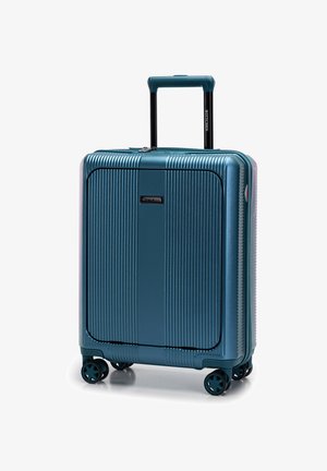 Valise coquée en teal avec texture rainurée verticale, poignée rétractable et quatre roues pour la mobilité. Comprend une étiquette de marque sur le devant.