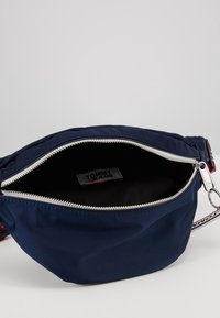 Borsa a cintura in nylon blu navy con zip argentata, dotata di una fodera nera e un'etichetta Tommy Jeans all'interno. Accentuata da una tracolla multicolore.