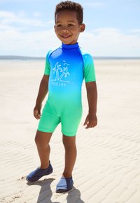 Muta da bambino a maniche corte con sfumatura blu e verde, con grafica di palma e scritta "BEACH LIFE". Abbinata a scarpe da acqua navy.