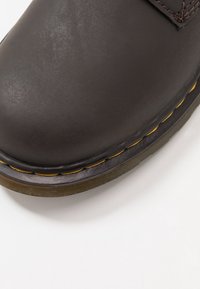 Chaussure en cuir marron avec une texture lisse, bout arrondi et couture jaune contrastante le long du bord de la semelle. Semelle extérieure en caoutchouc durable.