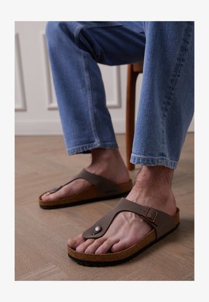 Zwarte flip-flopsandalen met een kurken zool, brede band en een gespdetail. Het oppervlak is glad en de voetbed lijkt gevoerd.
