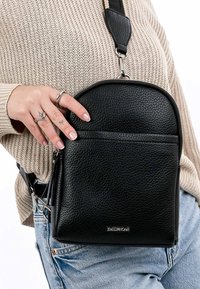 Black leather crossbody bag with a textured finish, rounded top, front zip pocket, and adjustable strap. Features branded hardware.