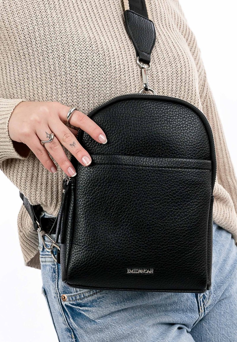 Black leather crossbody bag with a textured finish, rounded top, front zip pocket, and adjustable strap. Features branded hardware.