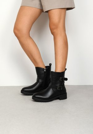 Stivaletti neri in pelle con punta rotonda, dettagli decorativi con cinturini e fibbie, zip laterale e suola in gomma spessa.