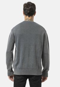 Pull en tricot gris avec un col et des poignets côtelés, arborant un motif texturé. La coupe est décontractée, avec un ourlet droit.