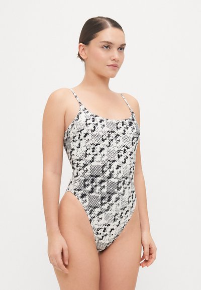 Maillot de bain imprimé serpent noir et blanc avec des fines bretelles, une coupe haute sur les jambes et une texture lisse, conçu pour une silhouette ajustée.