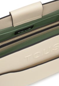 Borsa in pelle color crema con interno verde, caratterizzata da una cerniera dorata e dal logo "TOUS" in rilievo sull'esterno.