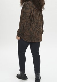 Brown patterned long-sleeve shirt with a gathered yoke, paired with black skinny jeans and black ankle boots. Soft fabric with a fluid silhouette.