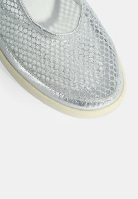 Silberne Netz-Slipper mit abgerundetem Zeh und einer weißen Gummisohle. Das strukturierte Obermaterial hat ein Wabenmuster mit metallischem Glanz.