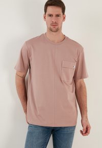 Kortärmad, ljusrosa t-shirt i bomull med rund halsringning och bröstficka. Har en sömlös frontdesign och avslappnad passform.