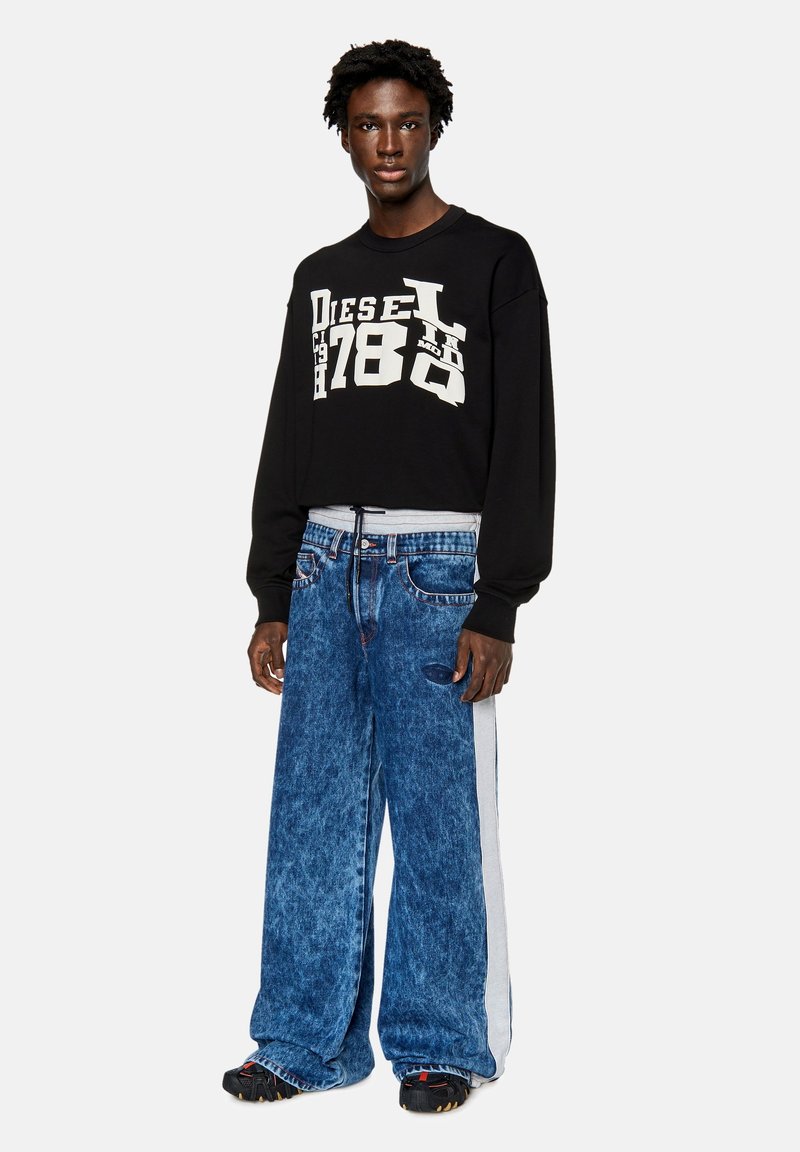 Felpa nera a maniche lunghe con stampata bold bianca "Diesel 1978". Indossata con jeans in denim a gamba larga blu chiaro con una striscia laterale bianca.