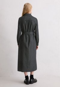 Długa sukienka z ciemnoszarego denimu z kołnierzykiem, długimi rękawami oraz wiązanym paskiem w talii. Charakteryzuje się prostym krojem i subtelną fakturą.
