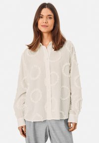 Lightweight, cream button-up shirt with ruffled circle appliqués. Long sleeves and a loose fit, featuring a classic collar and front buttons.