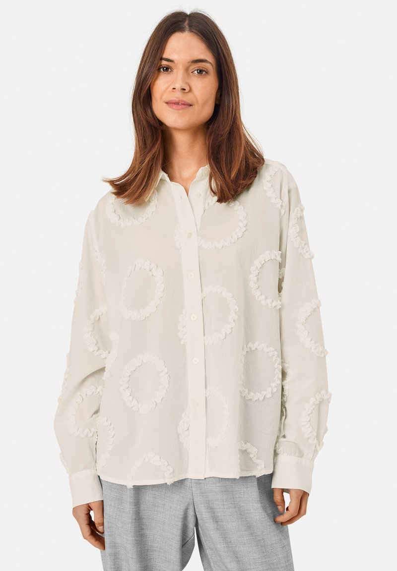 Lightweight, cream button-up shirt with ruffled circle appliqués. Long sleeves and a loose fit, featuring a classic collar and front buttons.