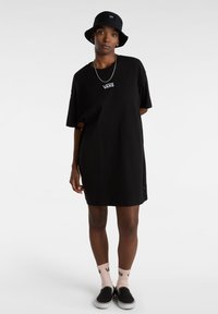 Sort bomulds t-shirt kjole med korte ærmer, Vans-logo på brystet, sidelæg, båret med sorte slip-on sko og pink strømper med Vans-branding.