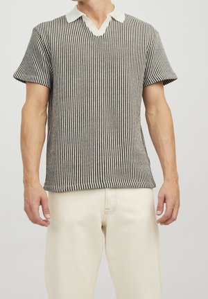 Polo à manches courtes noir et blanc à rayures avec un col en V et un col contrastant blanc, présenté avec un pantalon clair.