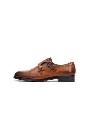 Zapato de vestir de cuero marrón con dos hebillas, punta redondeada y un tacón negro bajo. Textura suave con un acabado pulido y detalles de costura mínimos.