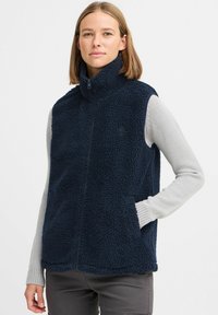 Mörkblå fleeceväst med hög krage, framzip och sidofickor. Texturerad, mjuk tyg med en bekväm utseende. Lagd över en ljus tröja.