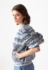 Adīta džemperis zil�ās toņos ar sarežģītām rakstu zīmēm, ribotām piedurknēm un apakšmalu, kā arī sānu kabatām. Mīksta tekstūra ar brīvu piegriezumu.