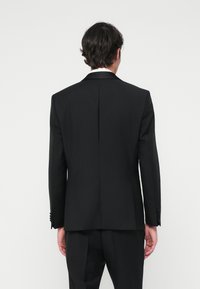Svart skrädarsydd kavaj med strukturerade axlar, enkel vent, och eleganta slag. Har knappmanchetter och en slät tygstruktur.