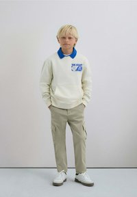 Sudadera blanca con cuello azul y logo, pantalones cargo beige, zapatillas blancas. Textura suave, diseño casual, ajuste relajado.