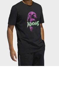 Schwarzes T-Shirt mit kurzen Ärmeln, das ein großes Grafikdesign eines lila Schädels und grünen Text zeigt. Der Stoff scheint weich und lässig geschnitten zu sein.