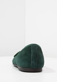 Scarpa flat verde in suede con forma rotonda, finitura texture, suola nera e un sottile dettaglio cucito sul retro.