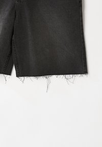 Shorts de mezclilla negra con dobladillo deshilachado, que presentan una tela texturizada y un corte recto. No hay adornos ni patrones visibles.