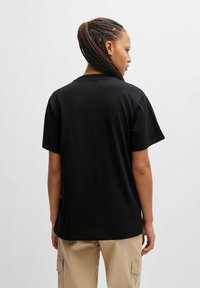 T-shirt in cotone nero con maniche corte, dalla vestibilità rilassata e dal design semplice. Il tessuto appare liscio, senza ulteriori motivi o accentuazioni.