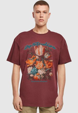 Burgunderfarvet bomulds t-shirt med blomster grafiktryk i orange, blå og hvid, med "M Studios" tekst omridset i rhinsten.