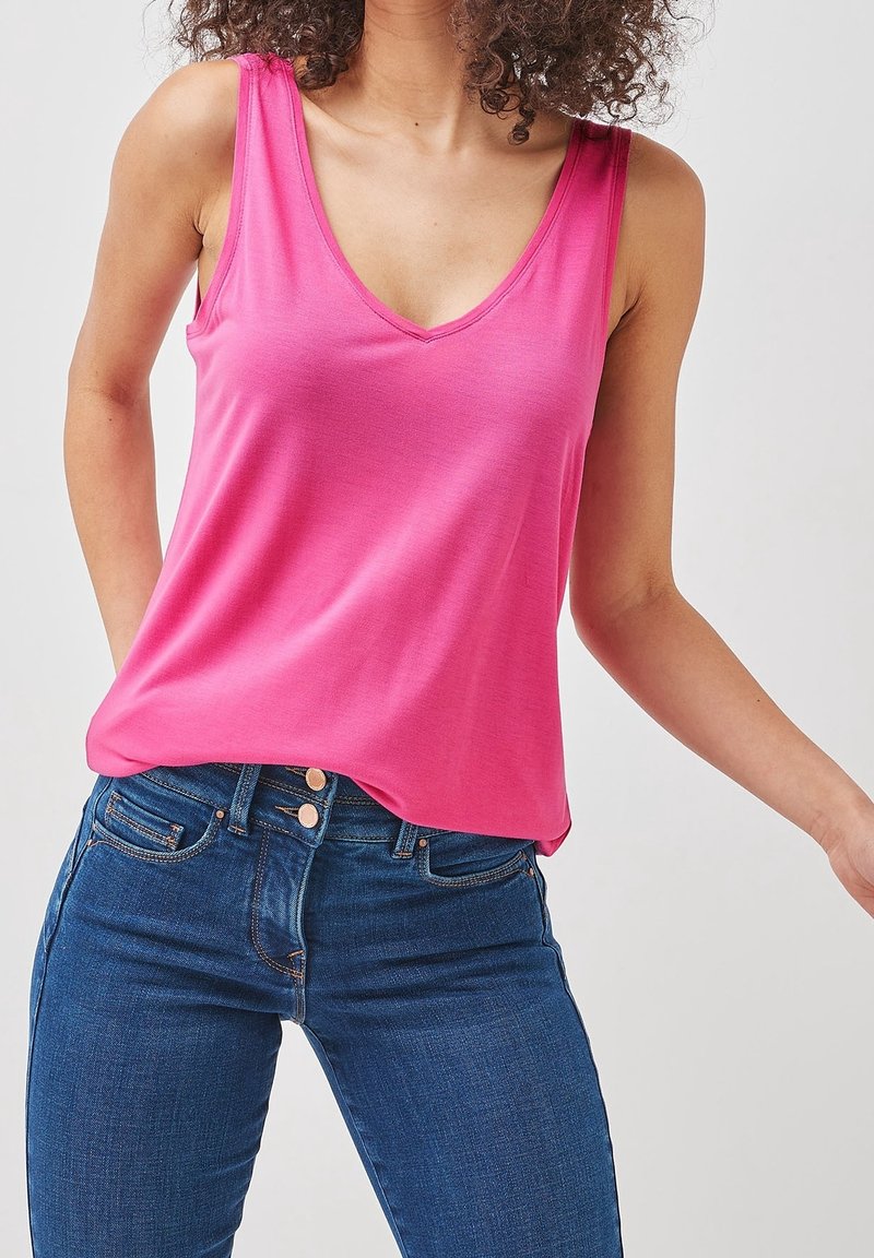 Pink sleeveless top with a deep V-neck, made of soft fabric, paired with dark denim jeans, featuring button details and a slim fit.