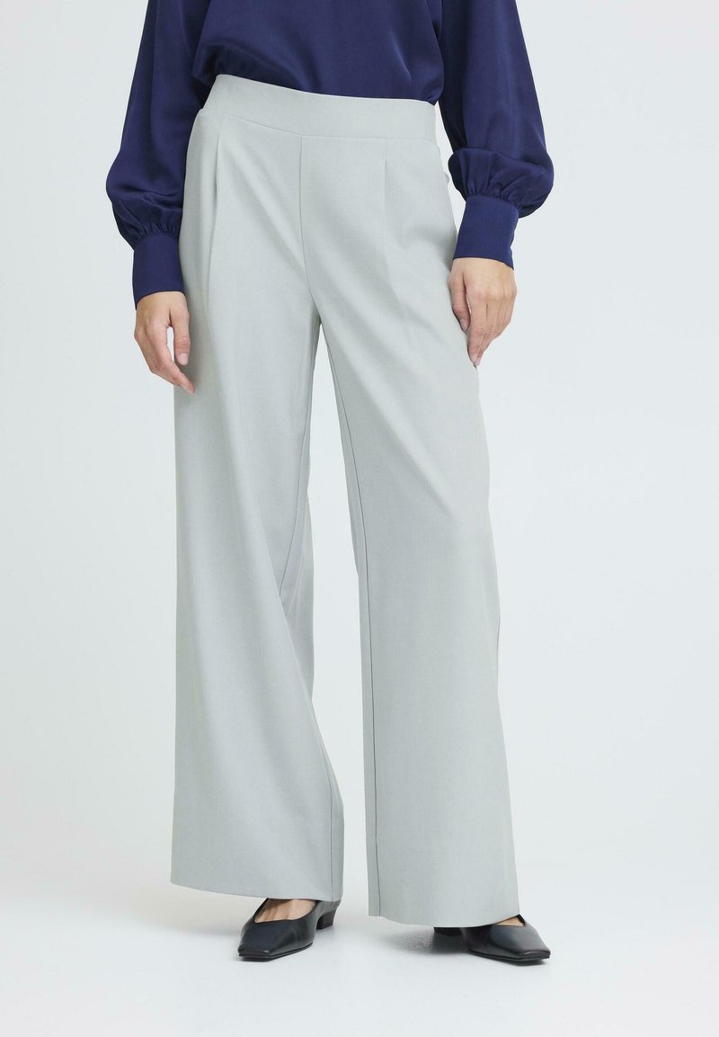 Šviesiai pilki, plačios kojos kelnės su aukštu juosmeniu ir plokščiu priekiu. Audinys atrodo lygus, derinamas su tamsiais, kvadratiniais bateliais.