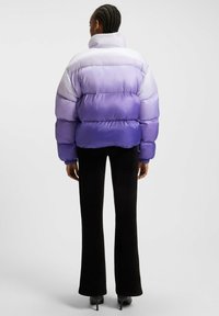 Puffjakke med en gradient fra lys til mørk lilla, højt krave og quiltet design. Sammen med sorte flagrende bukser og hæle.